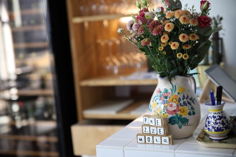 En vase med blomster og en dekoration med bogstaver, der staver "Prezzemolo," står på en hyggelig bordopsætning i en italiensk restaurant.